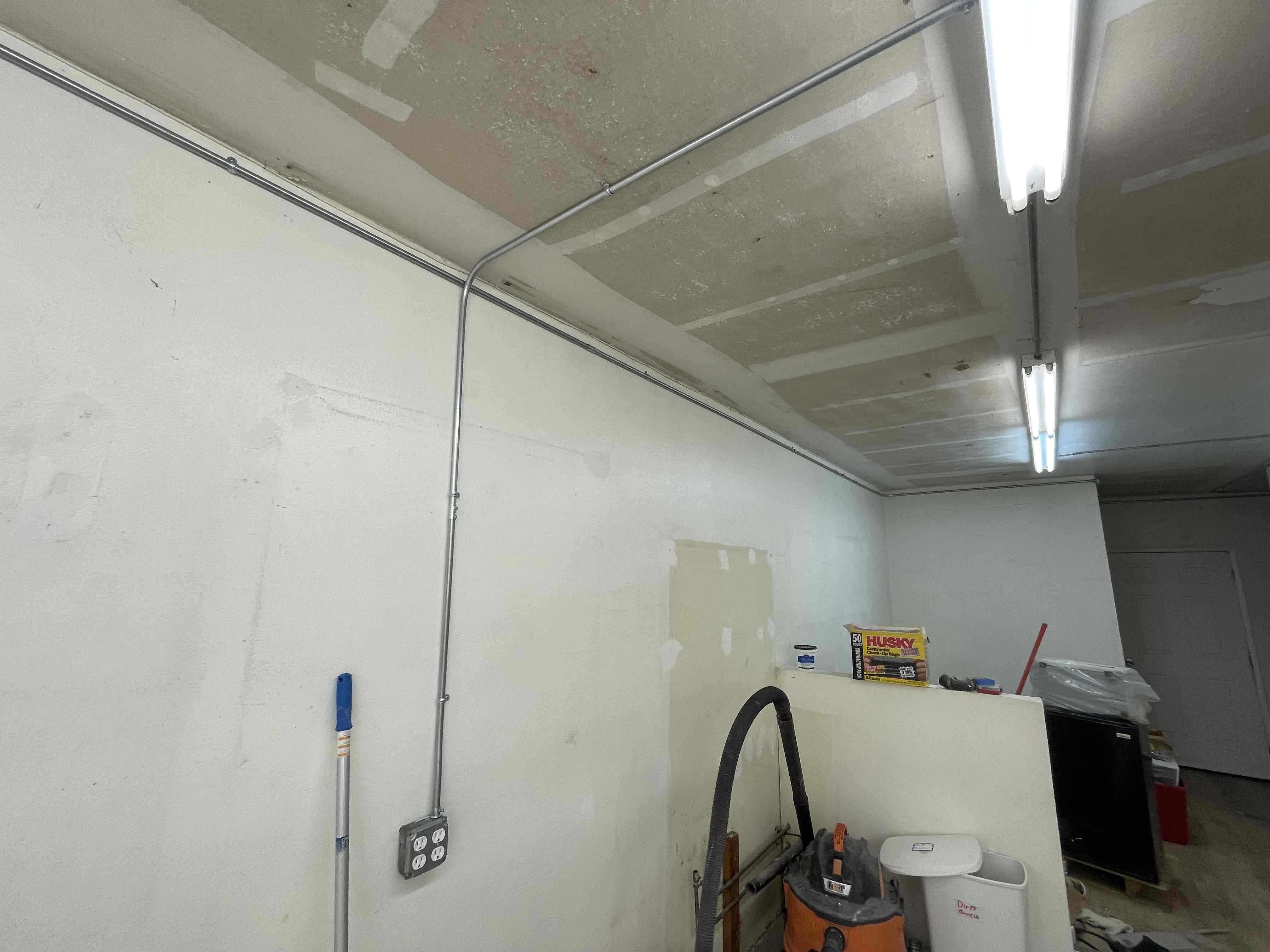 Surface electrical conduit, receptacle box, and illuminated lighting beside unfinished wall surfaces